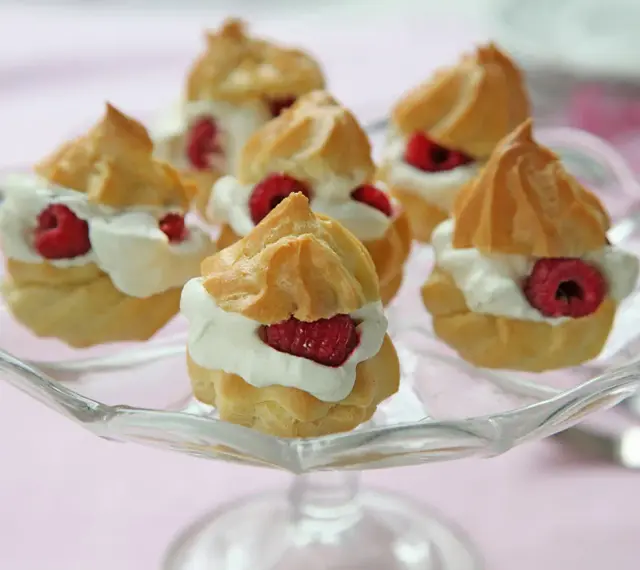Små petit choux fyllda med grädde och hallon på ett glasfat.