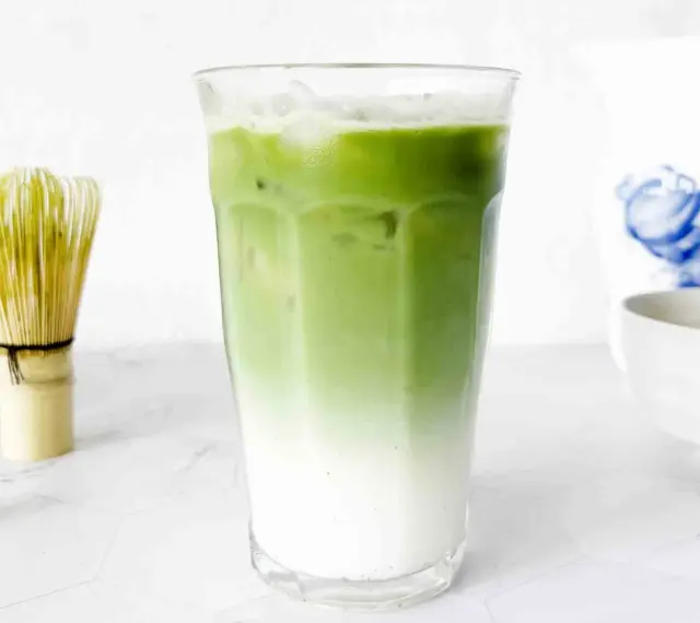 En isig matcha latte med lager av mjölk och grönt te. Bredvid står en bambuvisp, redo att blanda nästa goda dryck.