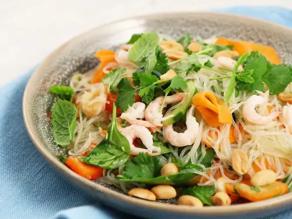 En läcker asiatisk nudelsallad med räkor, morötter, gurka, jordnötter och färska örter.